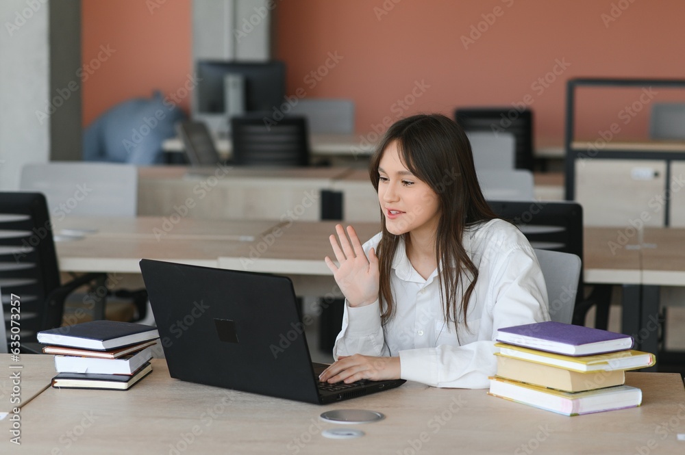 A beautiful caucasian female student is studying in college remotely. She is sitting with a laptop and a notepad and concentrated is watching a video conference lesson A beautiful caucasian female student is studying in college remotely. She is sitting with a laptop and a notepad and concentrated is watching a video conference lesson