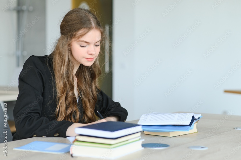 Teen girl studying with textbook writing essay learning in classroom. Teen girl studying with textbook writing essay learning in classroom.