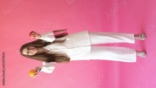 Happy girl dancing holding apple and orange on pink background, healthy way of life. Vegetarian girl portrait. Vertical 4k footage