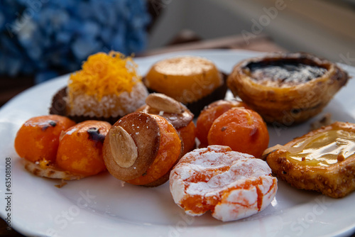 Mix of traditional Portuguese egg yolk sweets from Porto region on white plate with blue hydrangea on background.