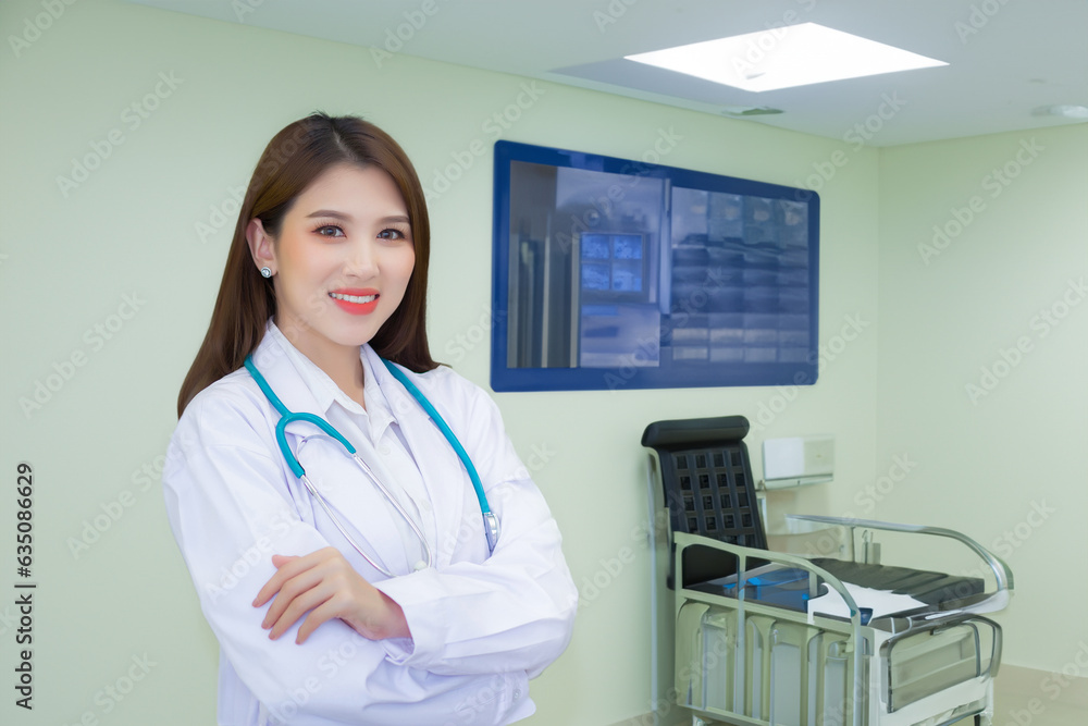 Professional young Asian woman doctor wearing white robe standing with arms crossed. Wearing a white robe and stethoscope happy and smile at examination room in hospital. Professional young Asian woman doctor wearing white robe standing with arms crossed. Wearing a white robe and stethoscope happy and smile at examination room in hospital.
