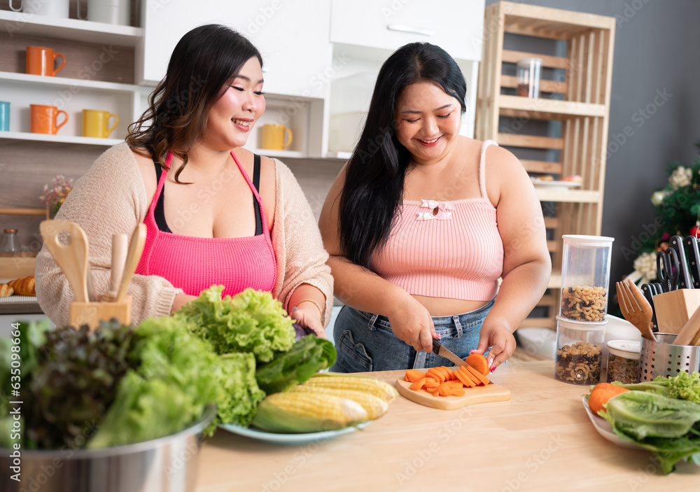Naklejka premium Happy Asia plus size woman cooking salad in kitchen at home 