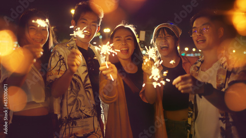 Group of Asian young man and woman having party on the beach at night.group of happy young Asian sitting and playing sparklers together with bokeh on tropical island beach at summer night.