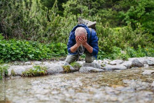 Active senior man washing his face in mountain stream.