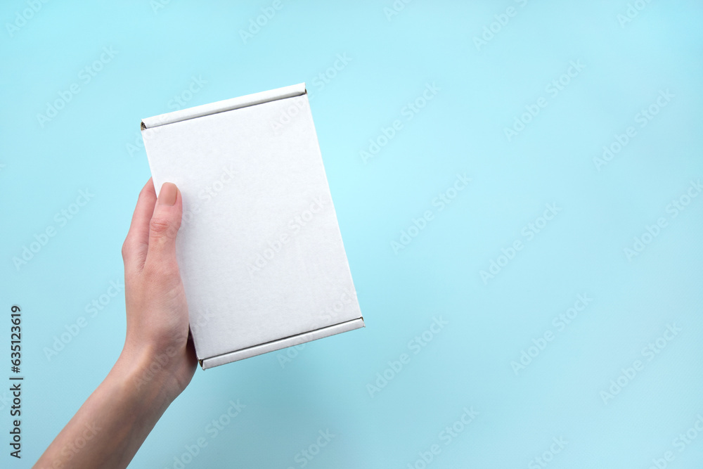 Female hands holding white package box on blue background. Female hands holding white package box on blue background.
