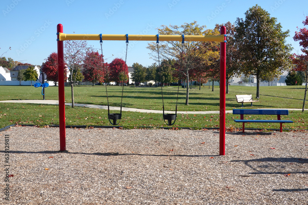 Toddler swings in a community playground with colorful posts and a wood chip ground Toddler swings in a community playground with colorful posts and a wood chip ground