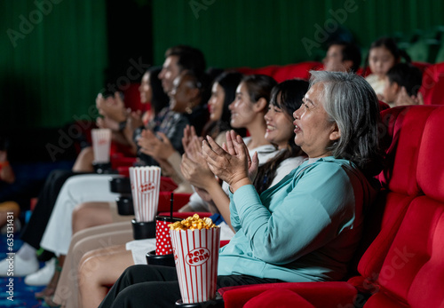 Side view of multiethnic and multigeneration people clap hands during watch movie together in cinema theater and they look happy in concept of enjoy entertainment on holiday.