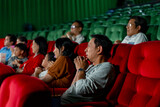 Wide shot of Asian man look scary or panic during watch movie with his family in cinema theater and other people sit beside also express the same action.