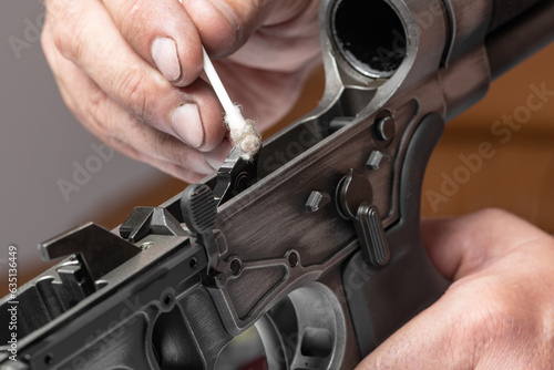 Man`s hands holding rifle parts details and cleaning the gun by cotton swab