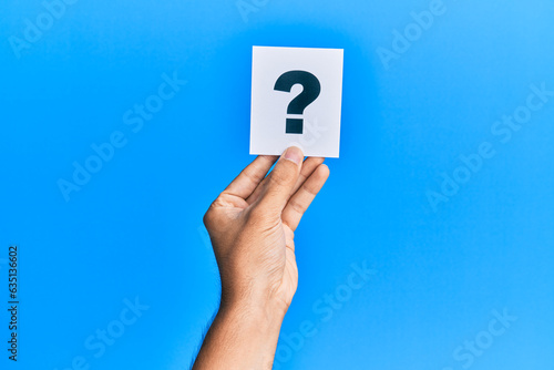 Hand of caucasian man holding paper with question mark over isolated blue background