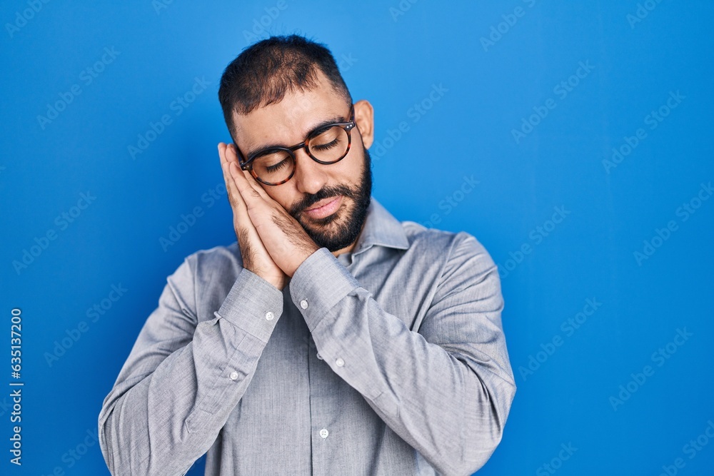Middle east man with beard standing over blue background sleeping tired dreaming and posing with hands together while smiling with closed eyes. Middle east man with beard standing over blue background sleeping tired dreaming and posing with hands together while smiling with closed eyes.
