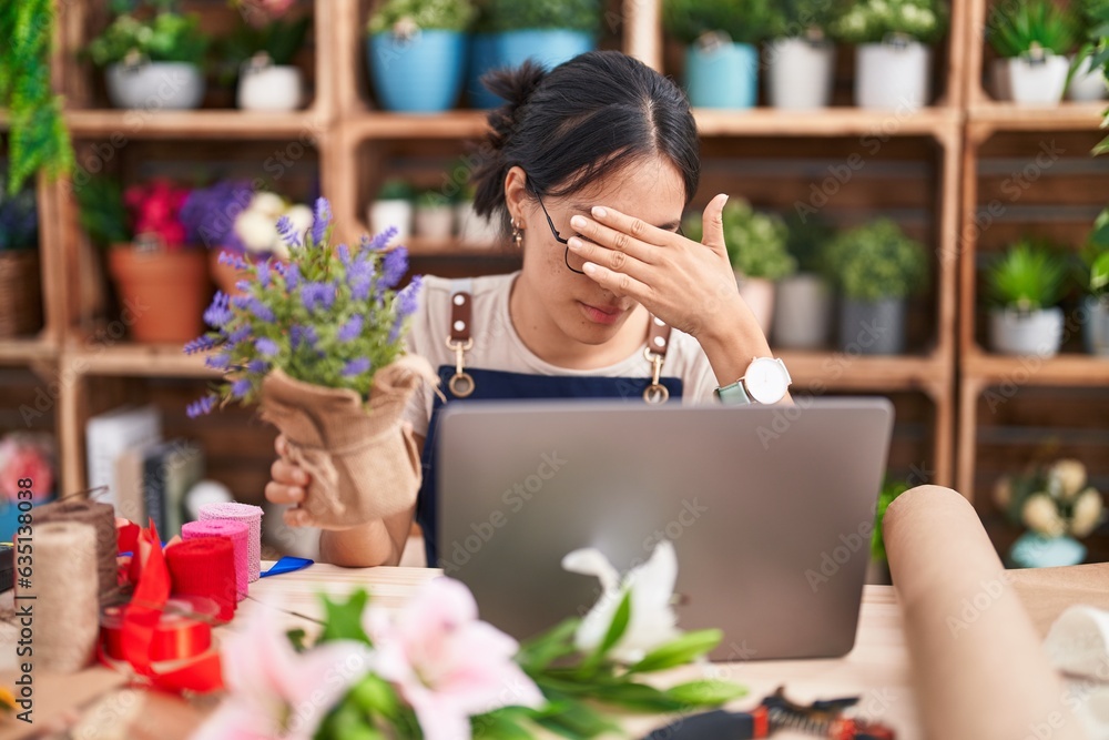 Young hispanic woman working at florist shop doing video call covering eyes with hand, looking serious and sad. sightless, hiding and rejection concept