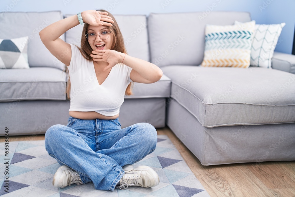Young caucasian woman sitting on the floor at the living room smiling cheerful playing peek a boo with hands showing face. surprised and exited Young caucasian woman sitting on the floor at the living room smiling cheerful playing peek a boo with hands showing face. surprised and exited