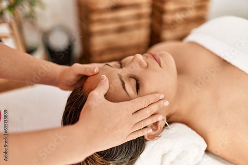 Young beautiful hispanic woman lying on table having head massage at beauty salon