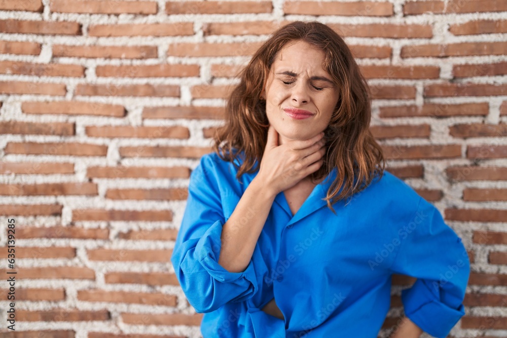 Beautiful brunette woman standing over bricks wall touching painful neck, sore throat for flu, clod and infection