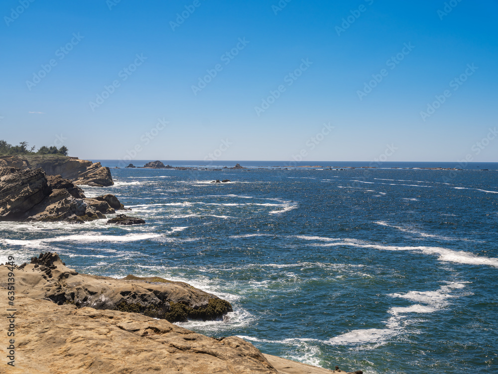 Rugged Rocky shoreline landscape along the Southern Oregon Coast with waves breaking on the jagged rocks and a bright blue sky with copy space. Rugged Rocky shoreline landscape along the Southern Oregon Coast with waves breaking on the jagged rocks and a bright blue sky with copy space.