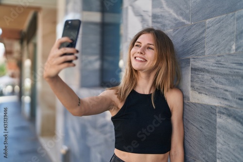 Young blonde woman smiling confident making selfie by the smartphone at street