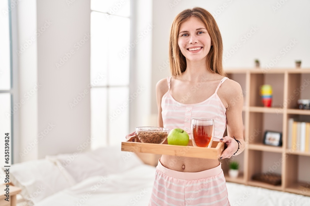 Young blonde woman holding healthy breakfast smiling at bedroom
