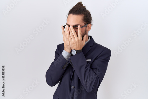 Hispanic man with beard wearing suit and tie with sad expression covering face with hands while crying. depression concept.