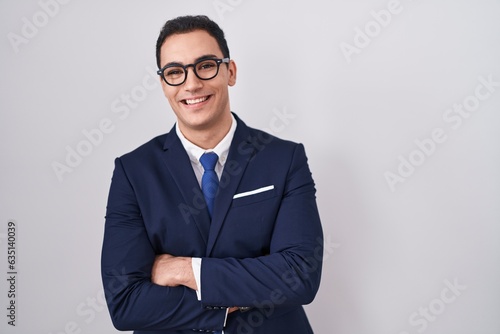 Young hispanic man wearing suit and tie happy face smiling with crossed arms looking at the camera. positive person.