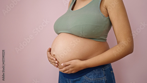 Young pregnant woman touching belly over isolated pink background © Krakenimages.com