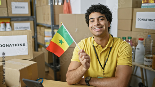 Young latin man volunteer holding senegal flag smiling at charity center