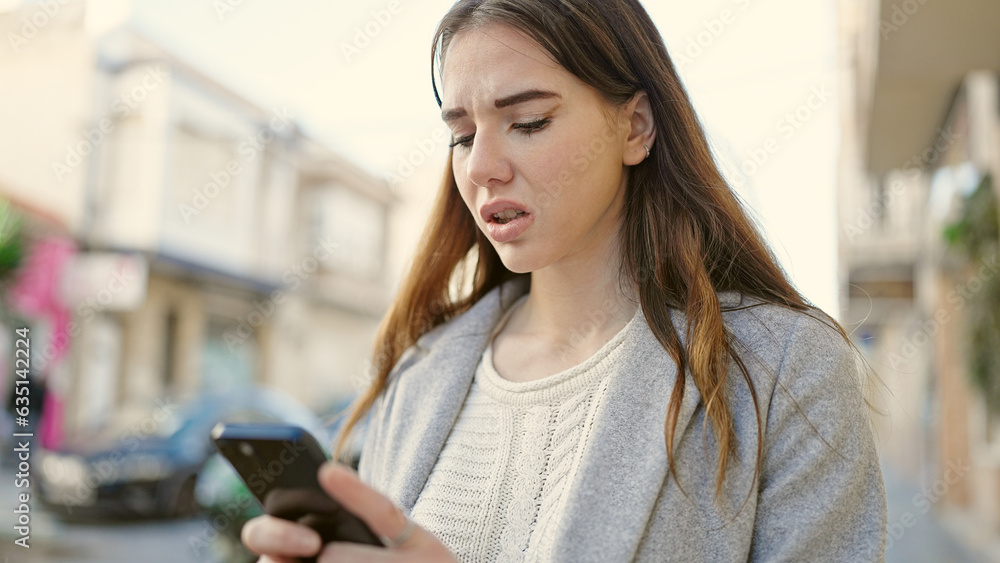 Young hispanic woman using smartphone looking upset at street
