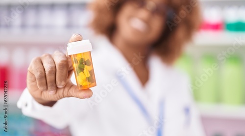 African american woman pharmacist smiling confident holding pills bottle at pharmacy