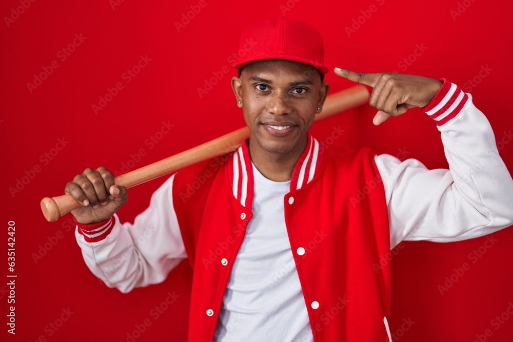 Young hispanic man playing baseball holding bat smiling pointing to head with one finger, great idea or thought, good memory Young hispanic man playing baseball holding bat smiling pointing to head with one finger, great idea or thought, good memory