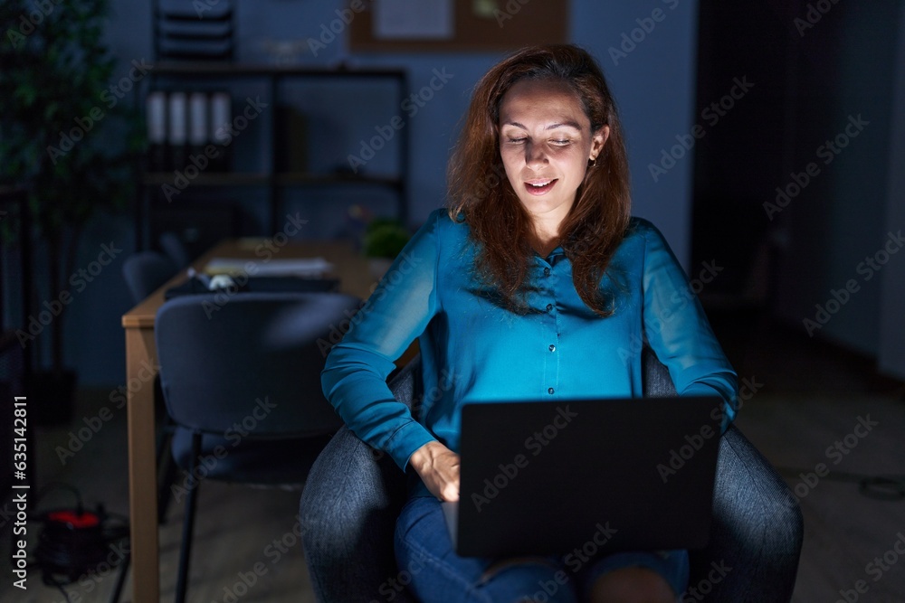 Brunette woman working at the office at night winking looking at the camera with sexy expression, cheerful and happy face. Brunette woman working at the office at night winking looking at the camera with sexy expression, cheerful and happy face.
