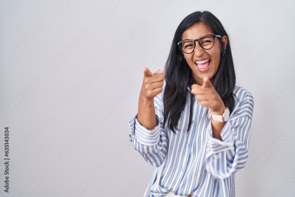 Young hispanic woman wearing glasses pointing fingers to camera with happy and funny face. good energy and vibes. Young hispanic woman wearing glasses pointing fingers to camera with happy and funny face. good energy and vibes.
