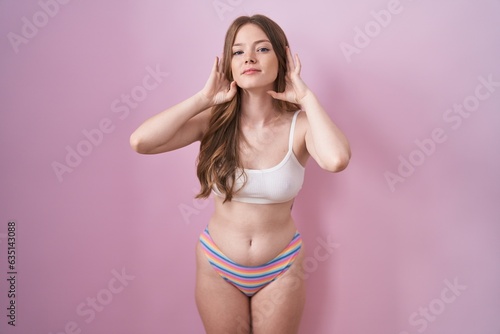 Caucasian woman wearing lingerie over pink background trying to hear both hands on ear gesture, curious for gossip. hearing problem, deaf © Krakenimages.com