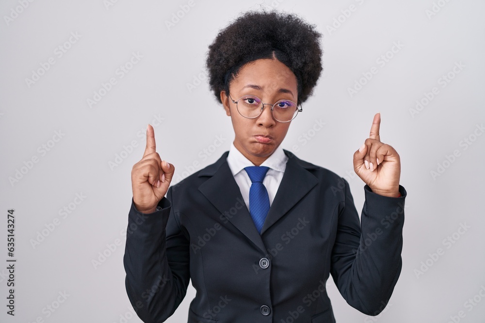 Beautiful african woman with curly hair wearing business jacket and glasses pointing up looking sad and upset, indicating direction with fingers, unhappy and depressed. Beautiful african woman with curly hair wearing business jacket and glasses pointing up looking sad and upset, indicating direction with fingers, unhappy and depressed.