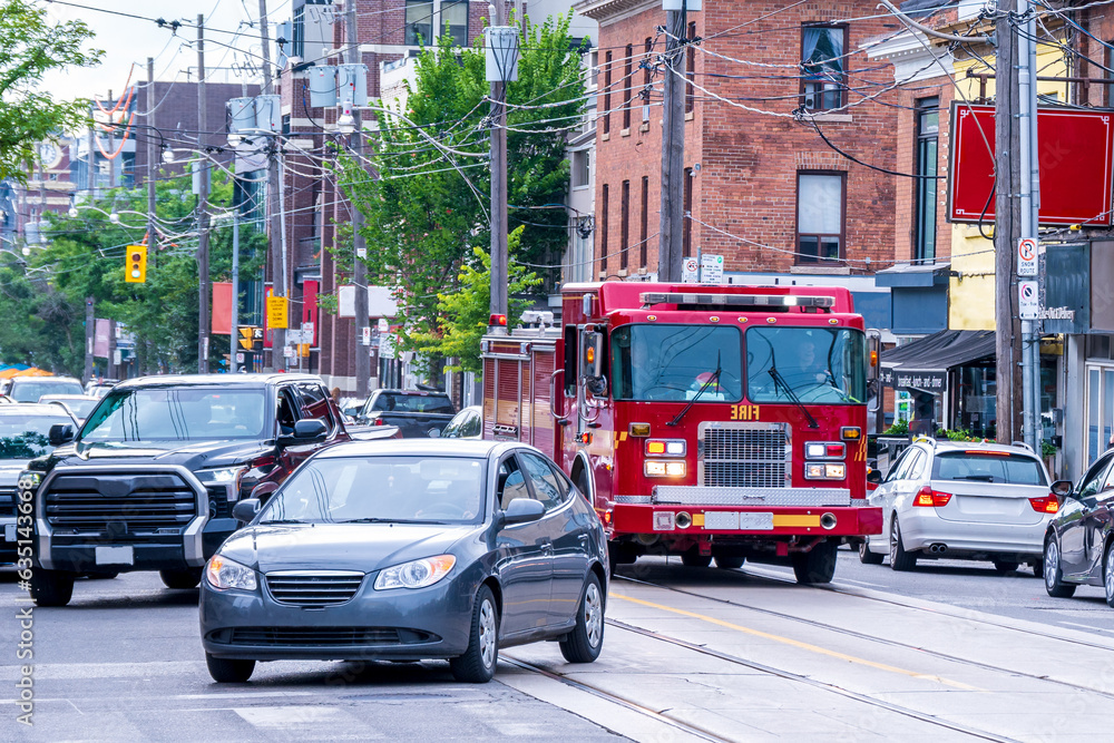 Naklejka premium emergency response: a fire truck manouvers through traffic on a busy street. shot in an older neighbourhood of toronto in the summer