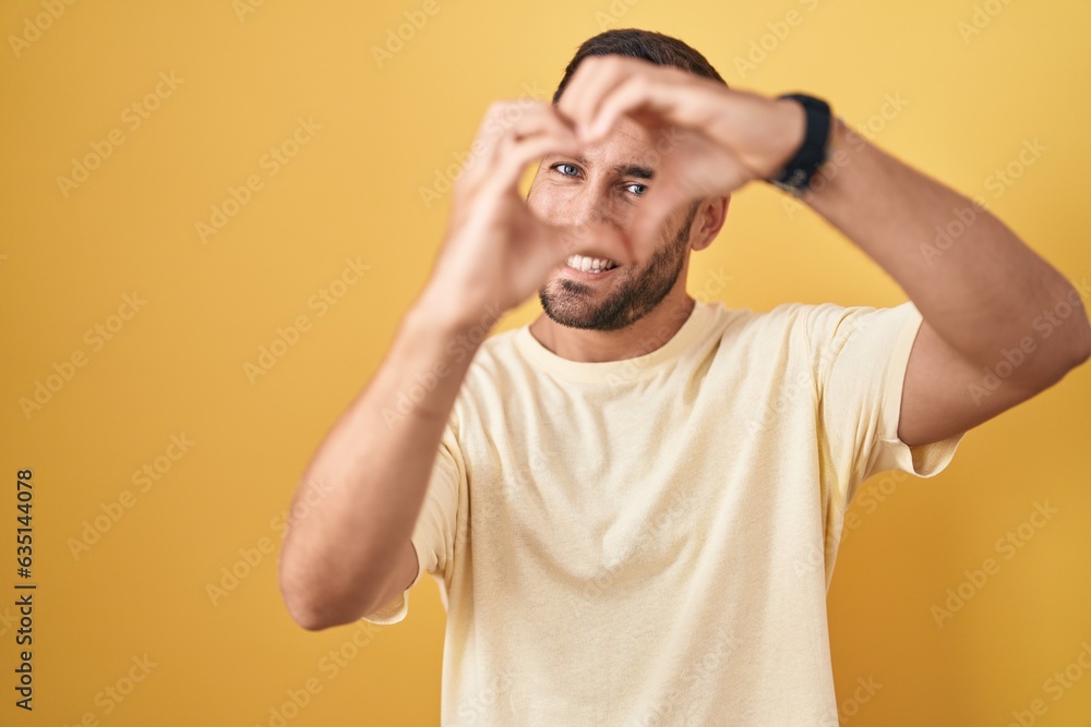 Handsome hispanic man standing over yellow background smiling in love doing heart symbol shape with hands. romantic concept. Handsome hispanic man standing over yellow background smiling in love doing heart symbol shape with hands. romantic concept.
