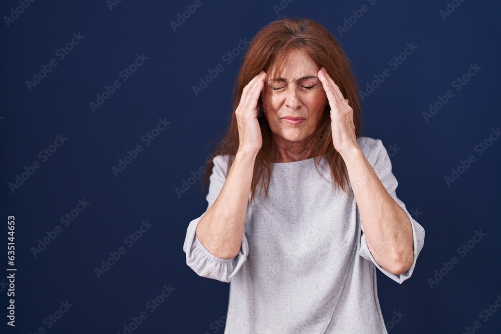 Middle age woman standing over blue background with hand on head for pain in head because stress. suffering migraine. Middle age woman standing over blue background with hand on head for pain in head because stress. suffering migraine.