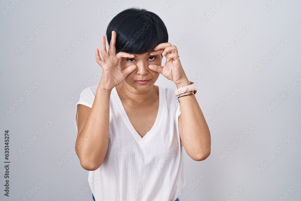Young asian woman with short hair standing over isolated background trying to open eyes with fingers, sleepy and tired for morning fatigue Young asian woman with short hair standing over isolated background trying to open eyes with fingers, sleepy and tired for morning fatigue