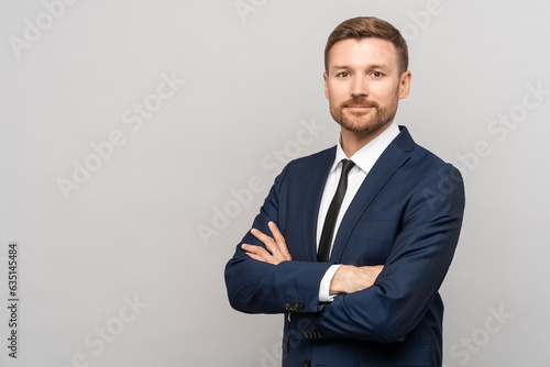 Successful trader man in business suit on studio gray background. Caucasian bearded young man folded arms over chest. Manager, director of company, successful businessman, investor, influential person