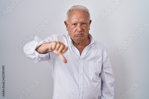 Senior man with grey hair standing over isolated background looking unhappy and angry showing rejection and negative with thumbs down gesture. bad expression.