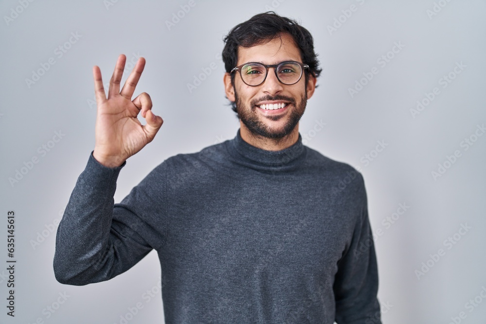 Handsome latin man standing over isolated background smiling positive doing ok sign with hand and fingers. successful expression. Handsome latin man standing over isolated background smiling positive doing ok sign with hand and fingers. successful expression.
