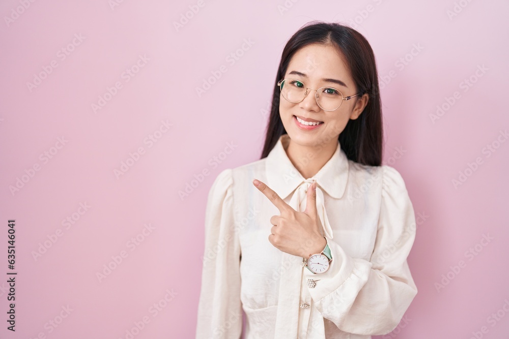 Young chinese woman standing over pink background cheerful with a smile of face pointing with hand and finger up to the side with happy and natural expression on face Young chinese woman standing over pink background cheerful with a smile of face pointing with hand and finger up to the side with happy and natural expression on face