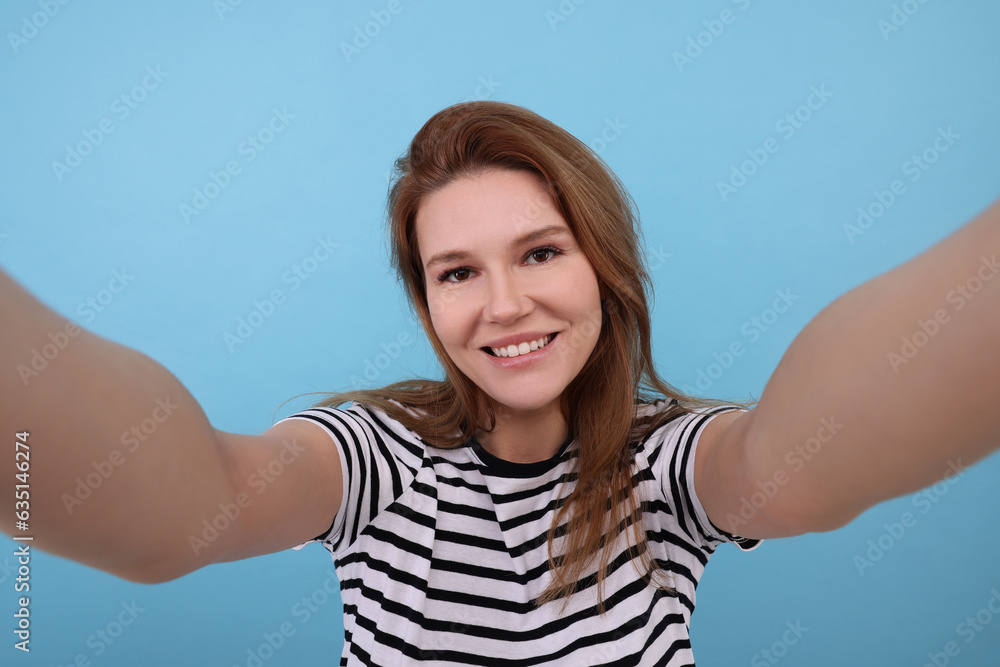 Beautiful woman taking selfie on light blue background Beautiful woman taking selfie on light blue background