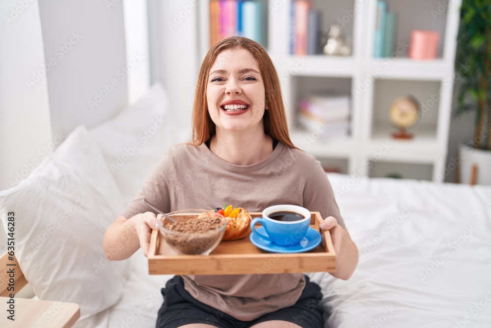 Redhead woman wearing pajama holding breakfast tray smiling and laughing hard out loud because funny crazy joke.