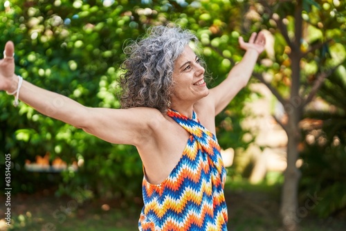 Middle age grey-haired woman smiling confident standing with arms open at park