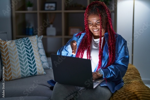 African american woman with braided hair using computer laptop at night smiling friendly offering handshake as greeting and welcoming. successful business. photo