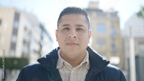 Young hispanic man standing with serious expression at street