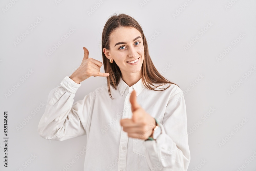 Young caucasian woman standing over isolated background smiling doing talking on the telephone gesture and pointing to you. call me. Young caucasian woman standing over isolated background smiling doing talking on the telephone gesture and pointing to you. call me.
