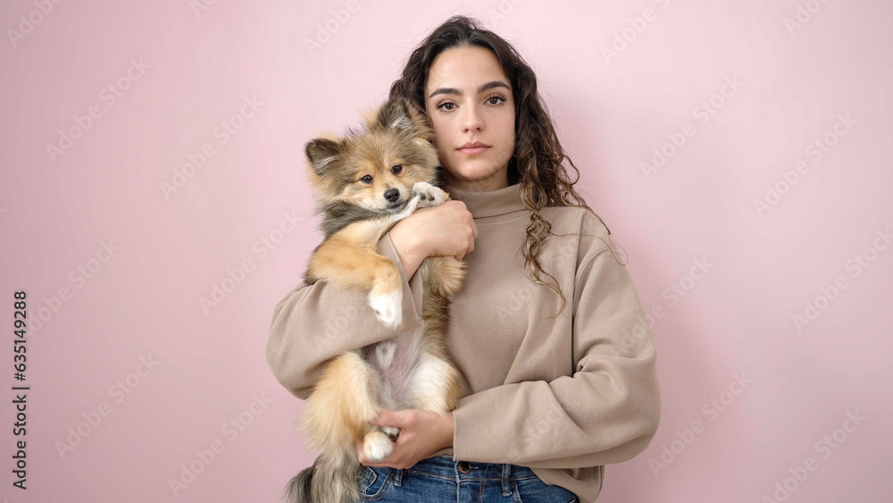 Young hispanic woman with dog standing with serious expression over isolated pink background Young hispanic woman with dog standing with serious expression over isolated pink background