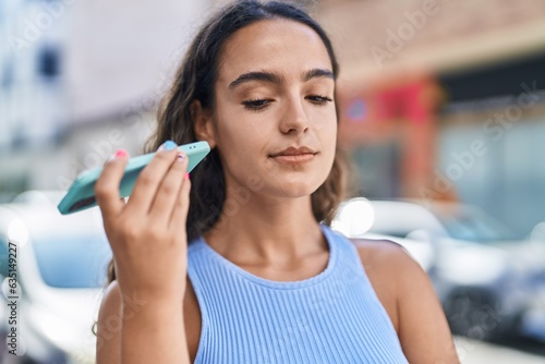 Young beautiful hispanic woman listening audio message by the smartphone at street