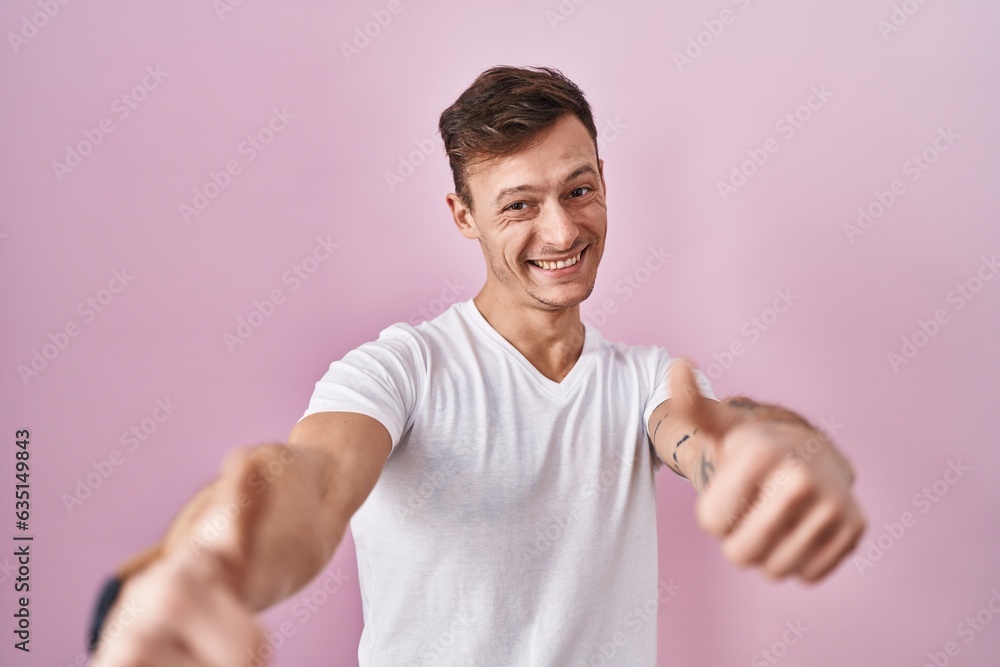 Caucasian man standing over pink background approving doing positive gesture with hand, thumbs up smiling and happy for success. winner gesture. Caucasian man standing over pink background approving doing positive gesture with hand, thumbs up smiling and happy for success. winner gesture.